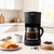Black filter coffee maker with glass jug on kitchen counter, shown with breakfast.