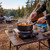 Progress single electric hot plate cooking pasta at campsite, tent and campfire in background