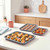 Three silver oven trays with roasted potatoes, cookies and mixed vegetables