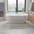 Freestanding white bathtub filled with foamy water in modern bathroom, grey bath mat in front