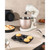 Cream stand mixer with whisk attachment on kitchen counter, shown with baked goods