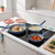 Set of three non-stick frying pans cooking chicken, creamy sauce, and tomatoes on a hob.