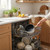 Cream saucepan with gold handle loaded into dishwasher in modern kitchen setting