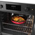 Oven interior with black control panel, showing a red pan cooking chicken and vegetables.