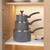 Stacked set of three grey non-stick saucepans with lids and handles in a kitchen cupboard