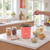 Red popcorn maker with kernels being poured in, bowls of popcorn on kitchen counter