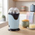 Electric popcorn maker in pastel blue on kitchen counter, shown with popcorn kernels and butter.