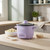 Purple rice cooker with glass lid on worktop, shown with cooked rice and uncooked rice nearby