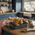 Roast chicken in enamel tray with vegetables and gravy jug in blue kitchen setting