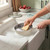 Hand washing a cream non-stick frying pan with sponge in soapy water at kitchen sink