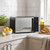 Black microwave oven on kitchen counter with lemons, olive oil, and sliced bread nearby