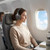 Woman wearing over-ear headphones seated on an airplane, sky view through window