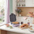Purple waffle maker open on kitchen counter with waffles, syrup and toppings nearby