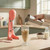 Glass of iced coffee being poured next to pink drink mixer on kitchen counter