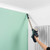 Cordless vacuum cleaning a ceiling corner in a modern room with pale green wall