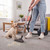 Vacuum cleaner removing pet hair from carpet beside a Labrador puppy in living room