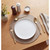Gold cutlery place setting with white plate and neutral placemat on wooden table