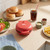 Red burger maker on kitchen counter with buns, salad, chips and sauces nearby