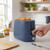 2-slice blue toaster with toast, hand pressing lever, on kitchen counter