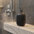 Black portable Bluetooth speaker with carry loop, water droplets, on bathroom counter.
