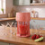 Red slushie maker with jug on kitchen counter, strawberries and lime beside glasses