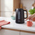 Black electric kettle with wood-effect handle, shown in use on a kitchen counter