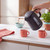 Modern black electric kettle pouring water into coral mugs on kitchen counter