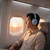 Man wearing blue wireless headphones on aeroplane, seated by window at sunset.