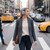 Woman in grey blazer wearing blue headphones crossing city street