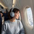 Person wearing silver headphones and grey jumper seated on airplane, clouds visible outside window