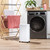White portable dehumidifier in laundry room beside drying rack and washing machine