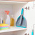 Grey dustpan and brush set with turquoise trim, stored in a cupboard with cleaning supplies.