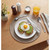 Breakfast setting with avocado toast and fried egg on plate, silver cutlery, glass of orange juice.