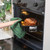 Black roasting tin with joint of meat and potatoes being taken from oven with green cloth