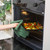 Hand placing tray of sliced vegetables into oven