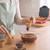 Churros being dipped in melted chocolate next to a churro maker in a kitchen setting