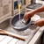 Hand washing grey non-stick frying pan under running tap in kitchen sink