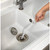 Hand cleaning a kitchen sink drain with a long white cleaning brush
