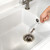 Hand cleaning a kitchen sink drain with a long white cleaning brush