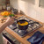 Hand stirring soup in black saucepan on gas hob, butternut squash and herbs on worktop