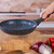 Black non-stick frying pan held over chopping board in kitchen, shown empty