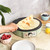 Green electric crepe maker on kitchen counter with fresh crepe, lemons, berries, and flour.