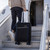 Black cabin suitcase with blue trim being wheeled up aircraft steps