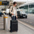 Black medium suitcase with front pocket and four wheels at an airport kerbside