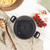 Grey speckled casserole pot with glass lid and black handles, top view