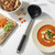 Black and silver soup ladle beside bowl of tomato soup and chopped vegetables