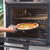 Hand placing margherita pizza on tray into oven