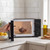 Black microwave oven with glass bowl of chocolate, door open on kitchen counter