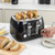 Black 4-slice toaster with bread slices, showing a person adjusting control knob