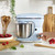 Light blue stand mixer with stainless steel bowl on kitchen counter, hand turning dial
